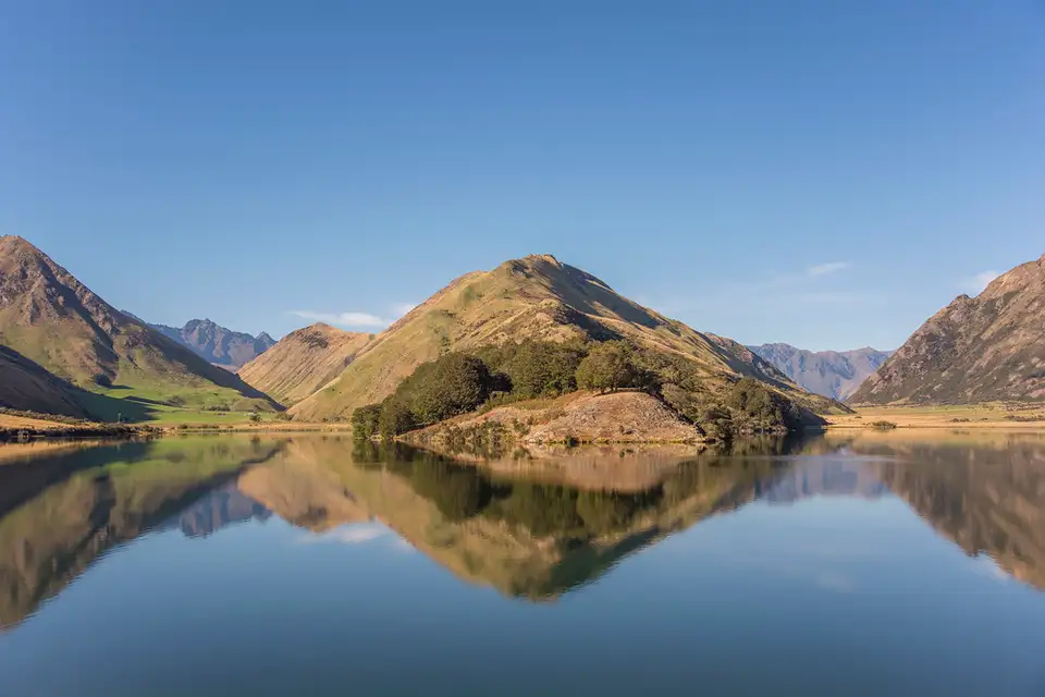 Moke Lake lying mirror-still with tussock hills reflected in the water