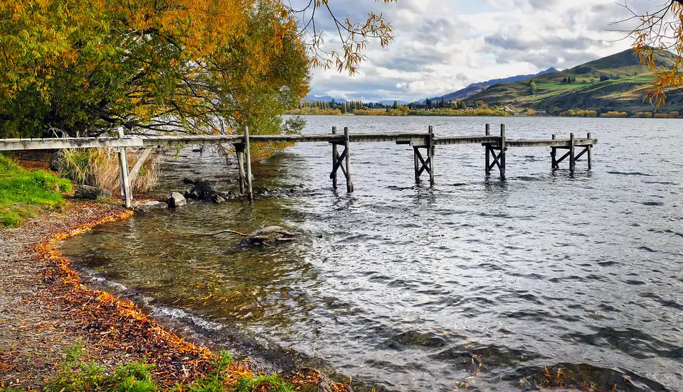 An old wooden jetty on Lake Hayes with autumn willows along the shore