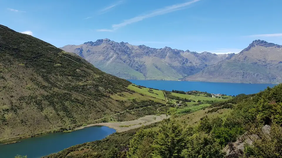 Lake Dispute sitting in a hollow of green hills with Lake Wakatipu and the mountains beyond