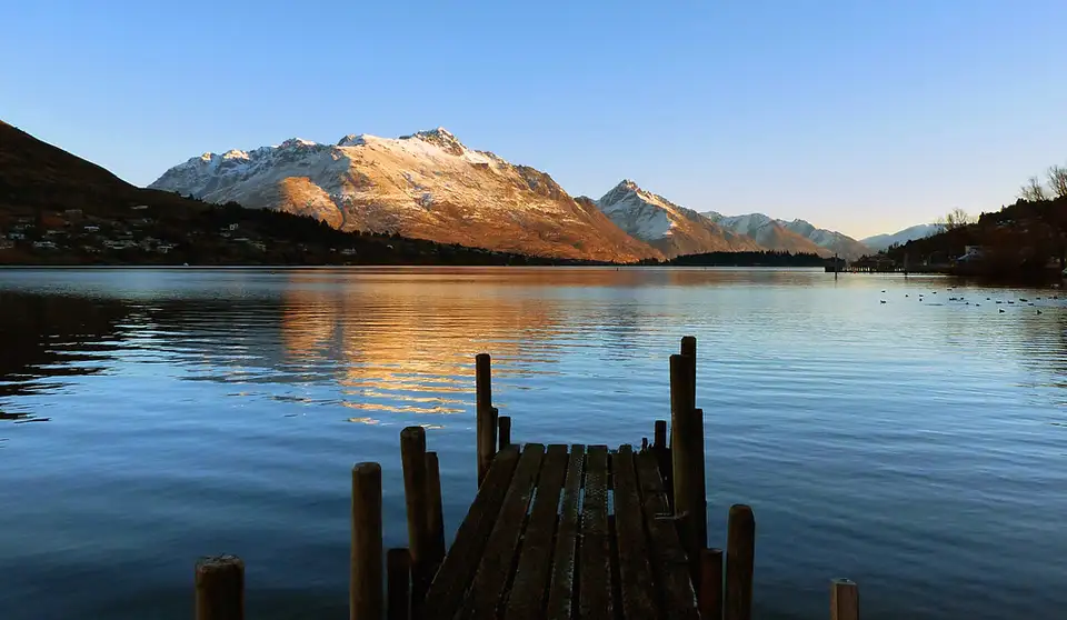 Old jetty piles standing in the Frankton Arm at dusk with mountains behind
