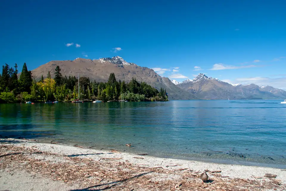 A shingle beach on Lake Wakatipu with snow-covered peaks across the water