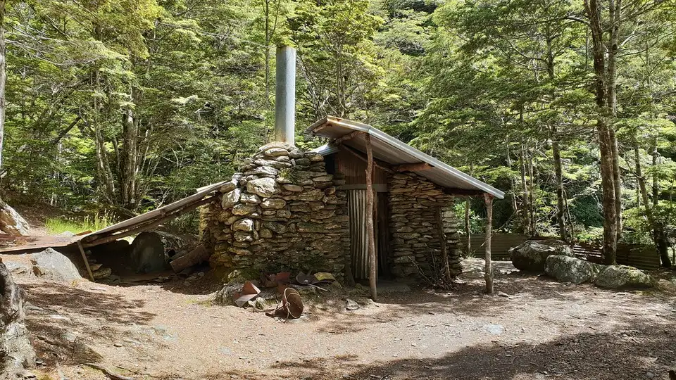 Sam Summers' Hut, a schist-walled hut with a corrugated iron roof and stone chimney, standing in beech forest