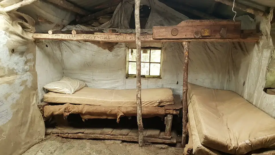 Inside Sam Summers' Hut: two bunks with old mattresses under a small window, with a rough timber post and beam