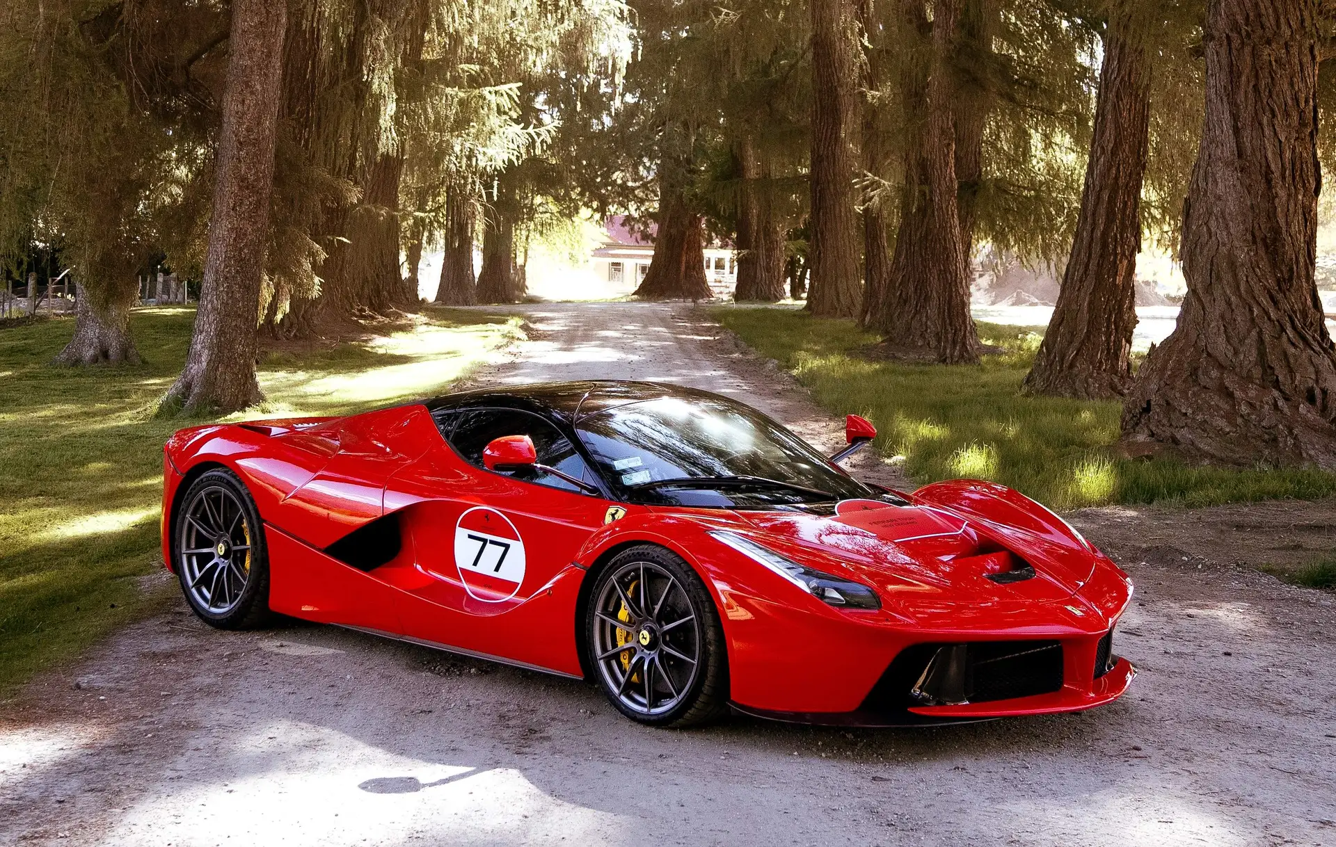 A red LaFerrari carrying race number 77 parked on the tree-lined gravel driveway at Ayrburn near Arrowtown