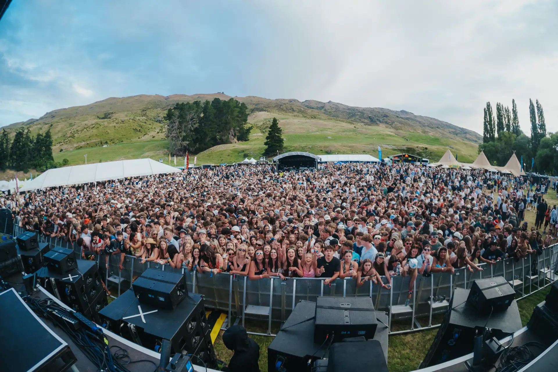 A packed festival crowd in front of the main stage at Rhythm and Alps, with the tussock hills of the Cardrona Valley rising behind