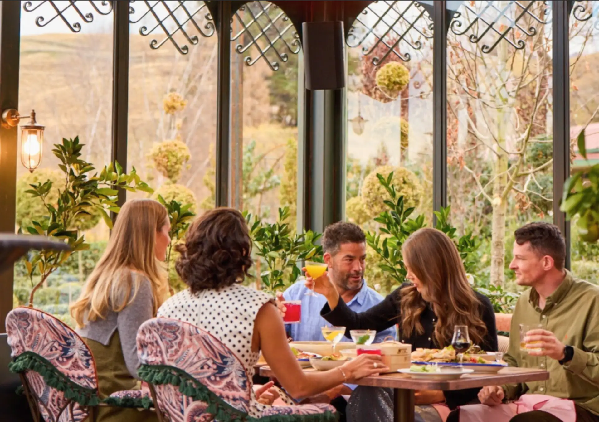 Five people at a round table in the glass conservatory at Billy's, with the Ayrburn gardens visible through the arched windows