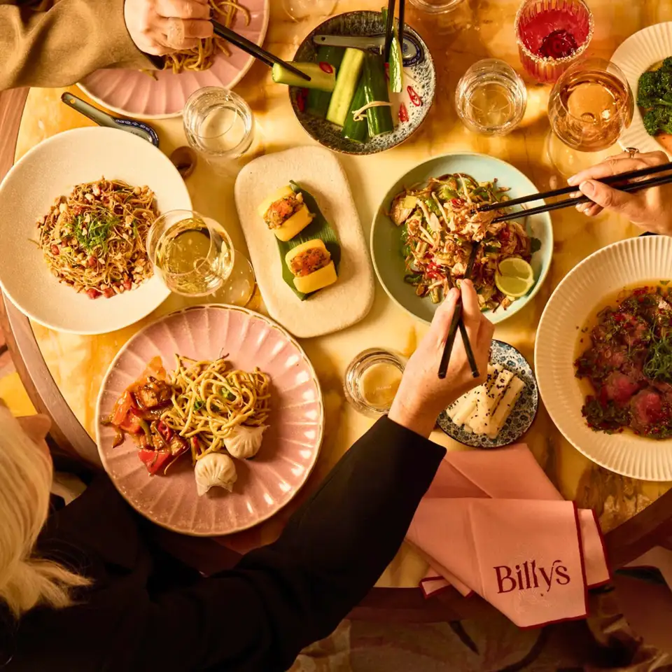 Overhead view of a shared Cantonese table at Billy's, with noodles, dumplings, pickled cucumber and beef being served with chopsticks