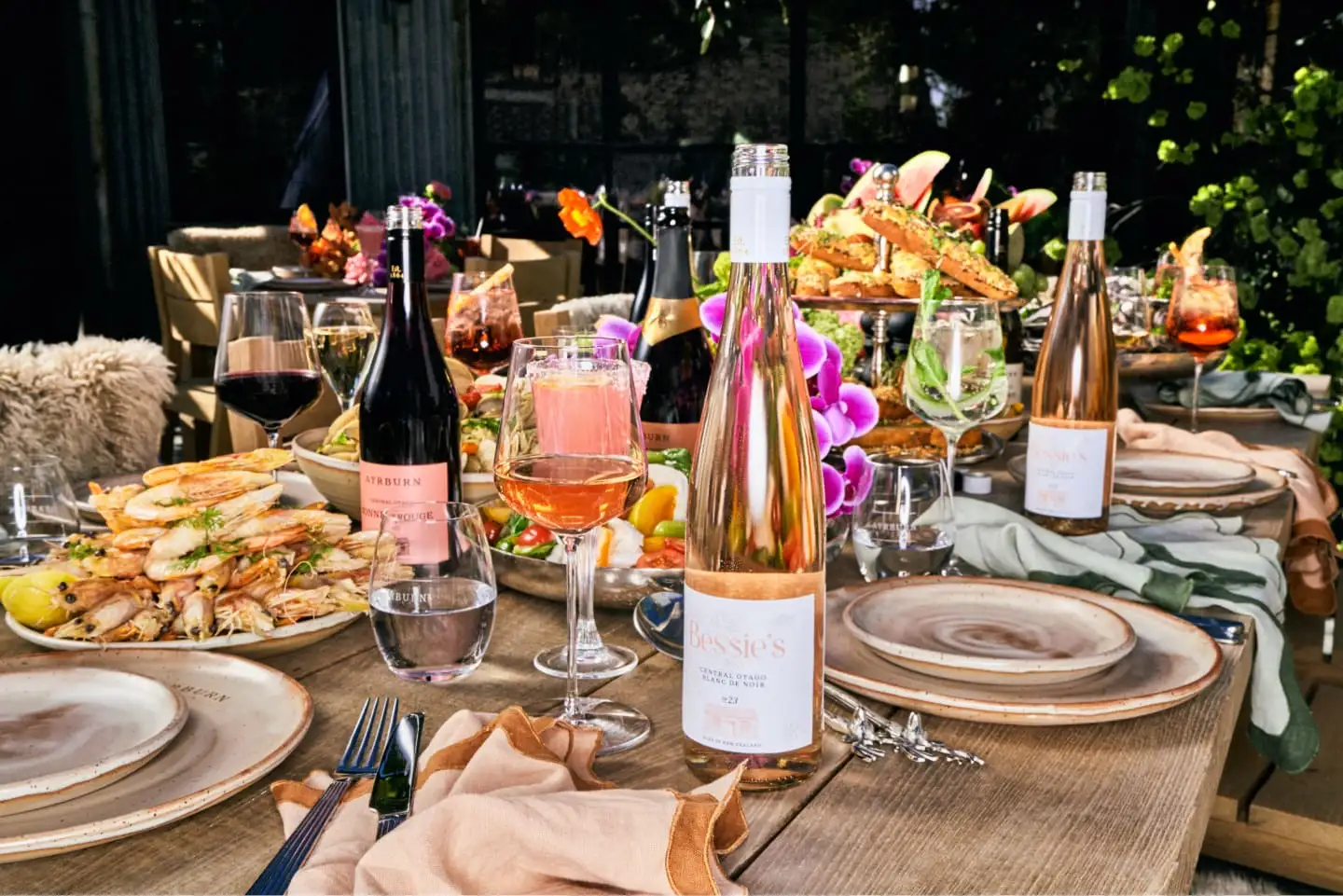 A long outdoor table at Ayrburn laid for lunch with prawns, salads, flowers and bottles of Central Otago wine