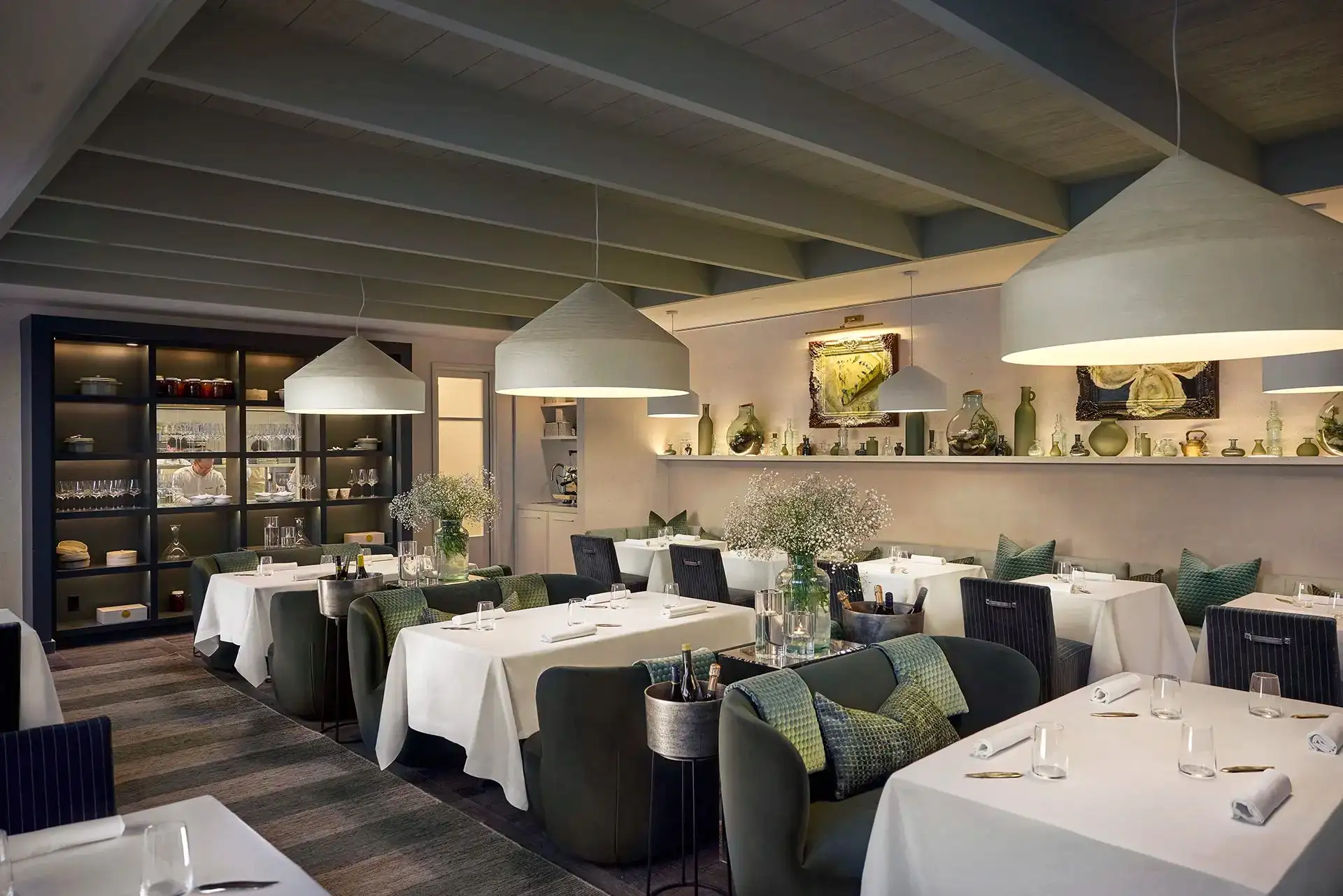 The dining room at Essence, with white-clothed tables set beneath a pitched timber ceiling and pendant lights.