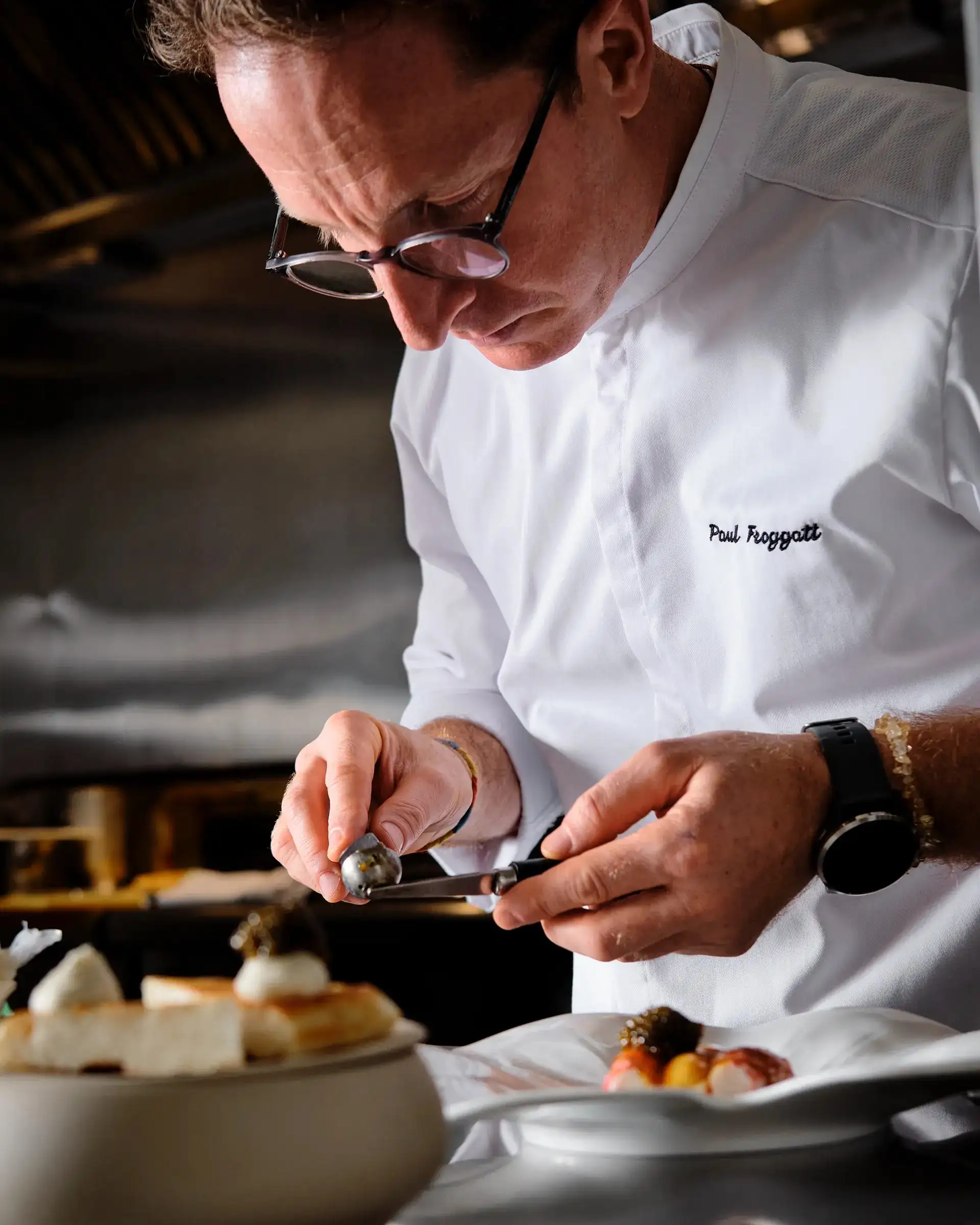 A chef in kitchen whites using tweezers to finish a plated course at Essence.