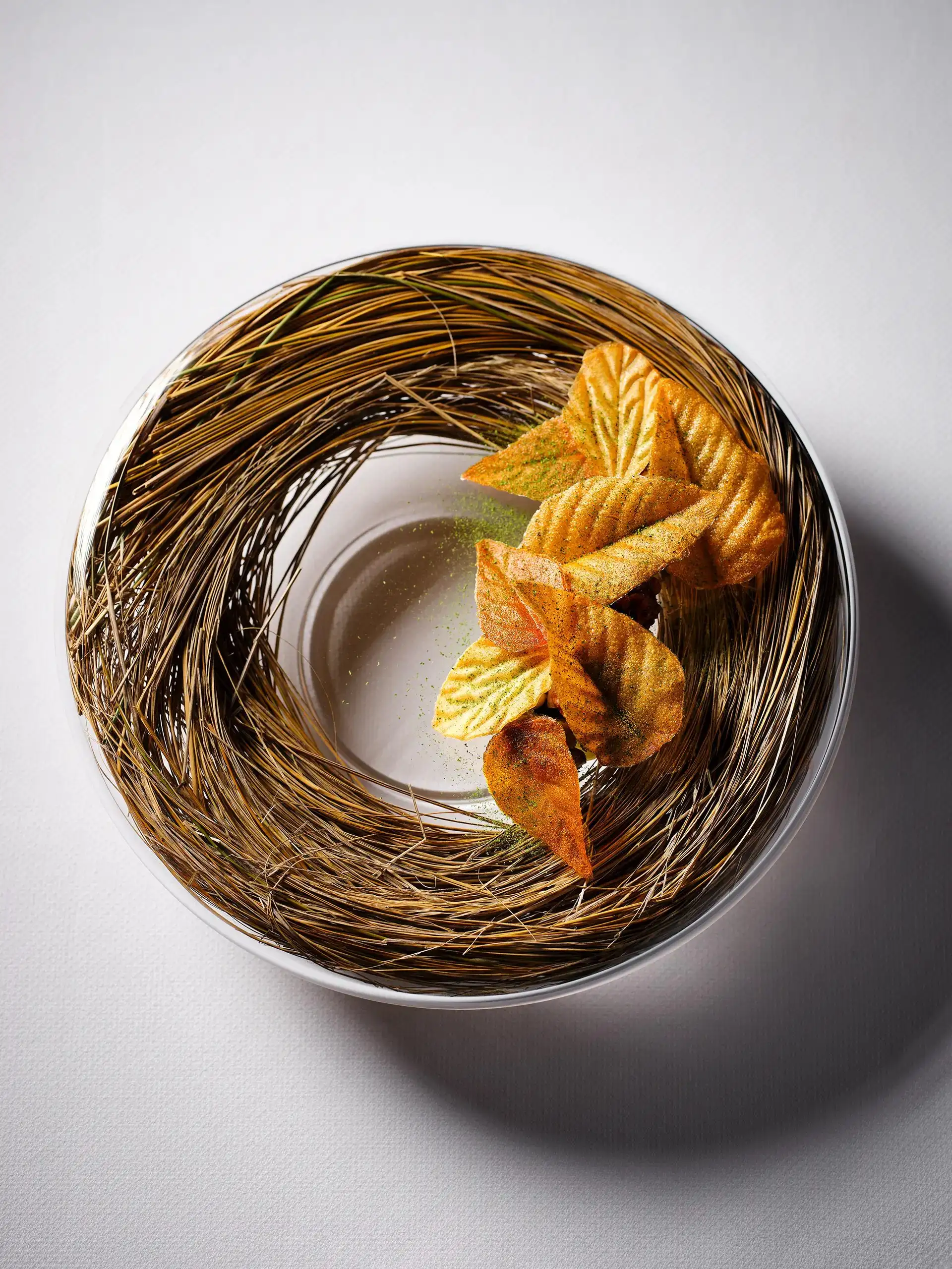 A course at Essence served in a woven twig nest, with folded pastry leaves around a pale centre.