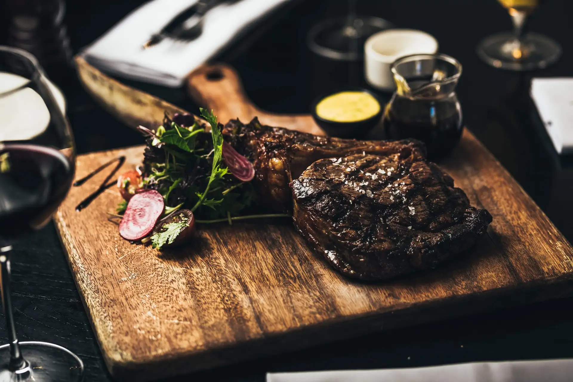 A grilled steak on a wooden serving board with sauces and a glass of red wine at Botswana Butchery.