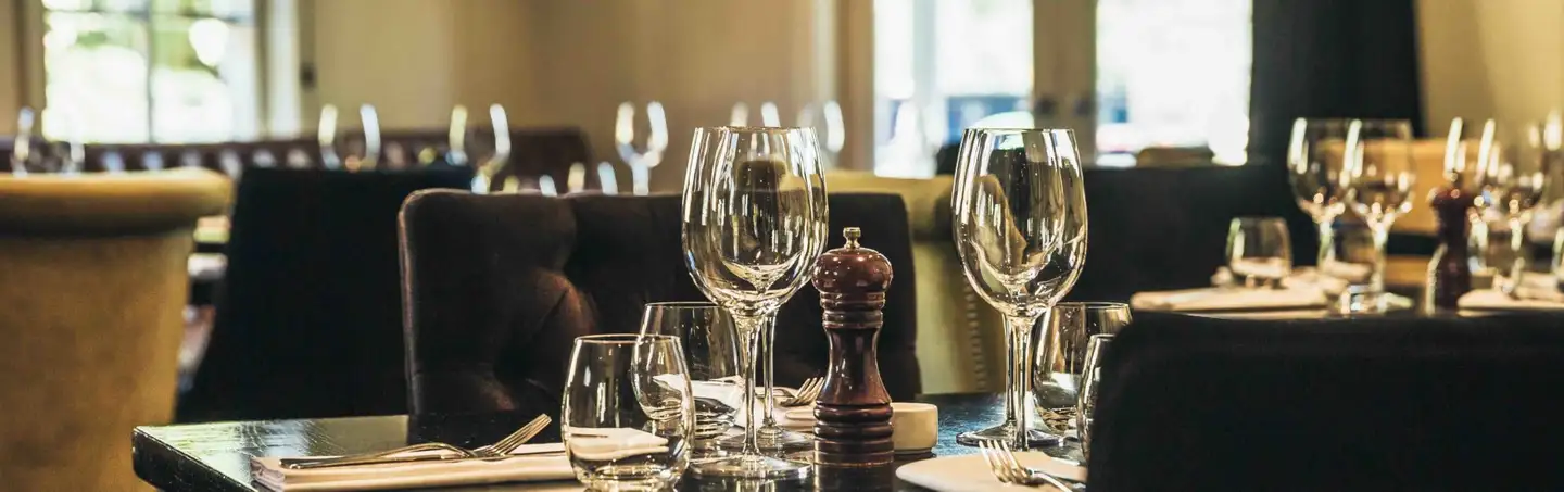A set table in the dining room at Botswana Butchery, with wine glasses, dark leather banquettes and a window beyond.