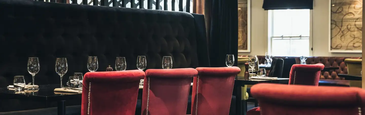 A private dining room at Botswana Butchery with red velvet chairs, a buttoned banquette and stone walls.