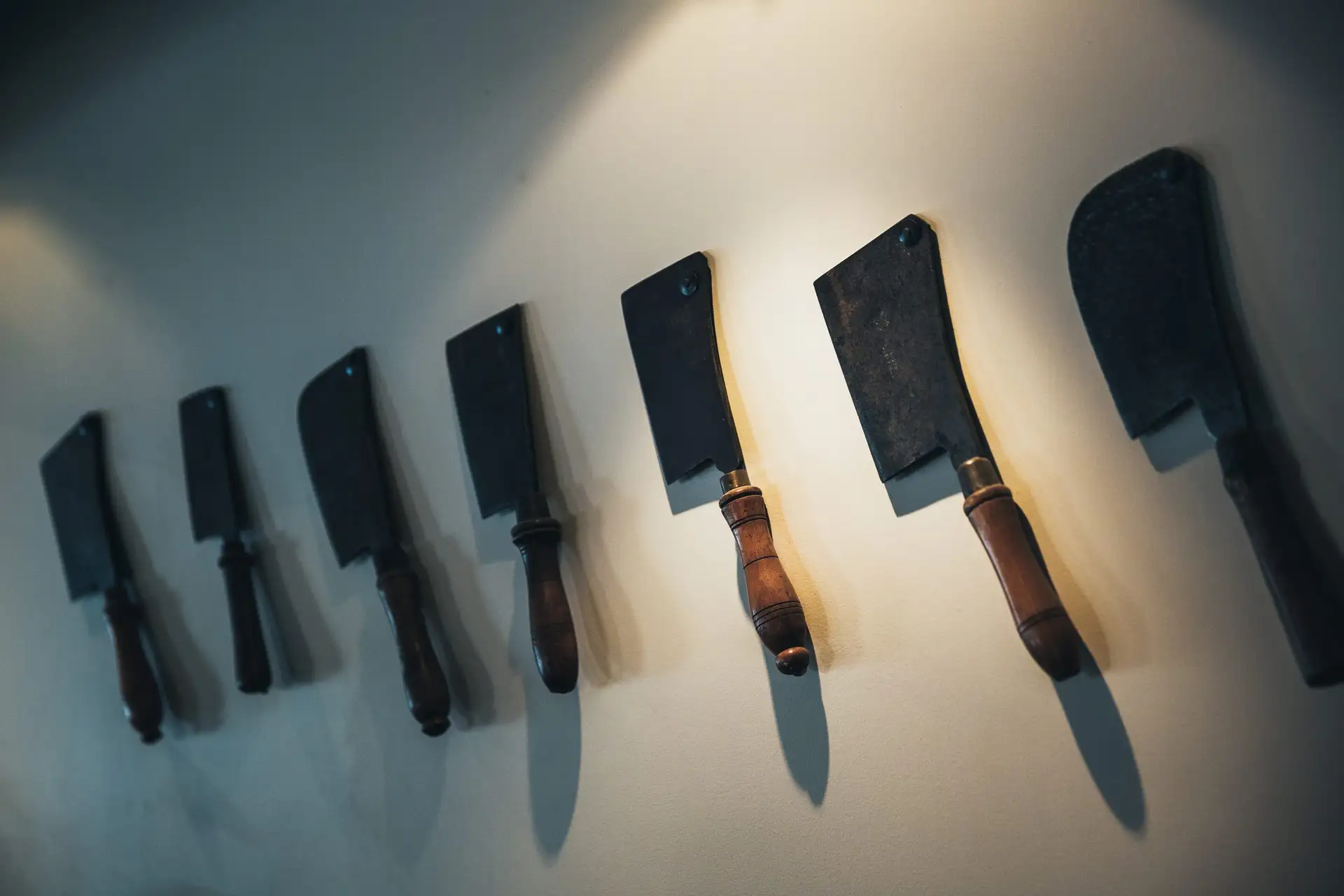 A row of butcher's knives and cleavers with wooden handles hanging on a pale wall at Botswana Butchery.