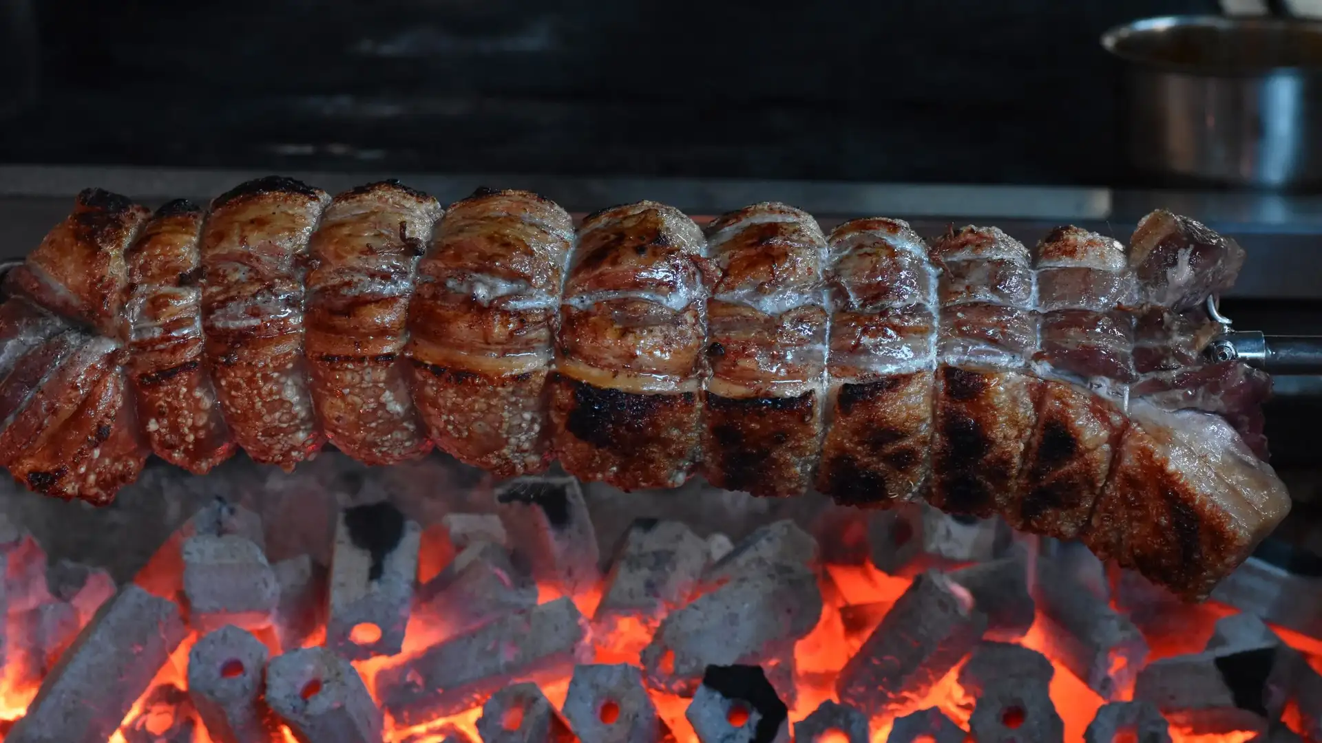 A long cut of rotisserie pork belly turning above glowing coals at Prospects.