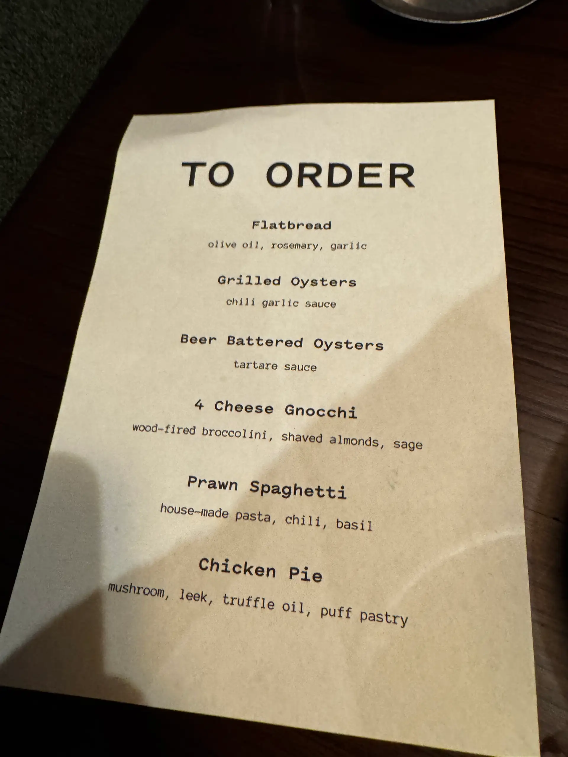 The printed To Order card on a table at Prospects, listing flatbread, grilled oysters, beer-battered oysters, four-cheese gnocchi, prawn spaghetti and chicken pie.