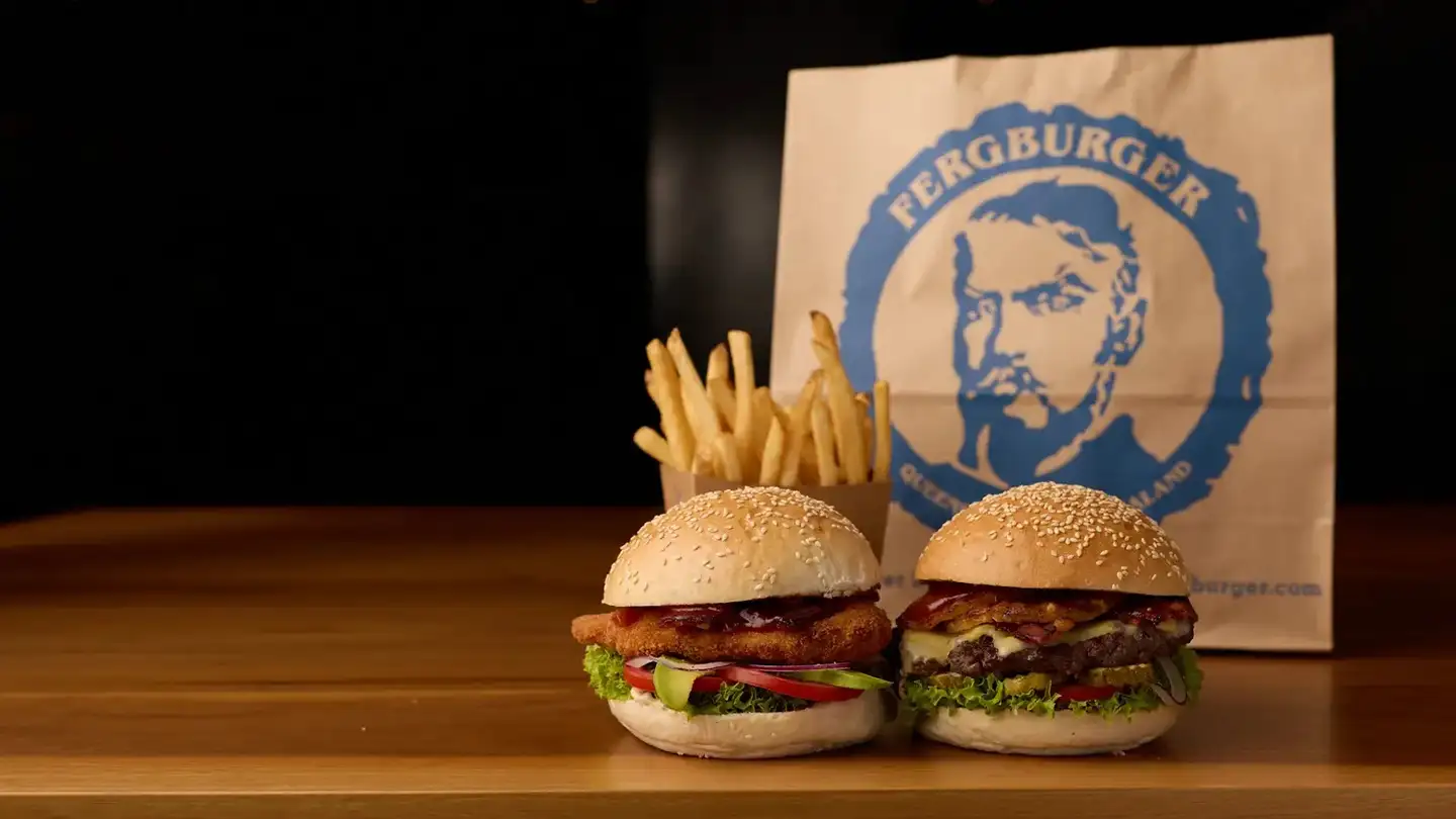 Two Fergburger burgers and a carton of fries on a wooden counter, with a Fergburger takeaway bag behind