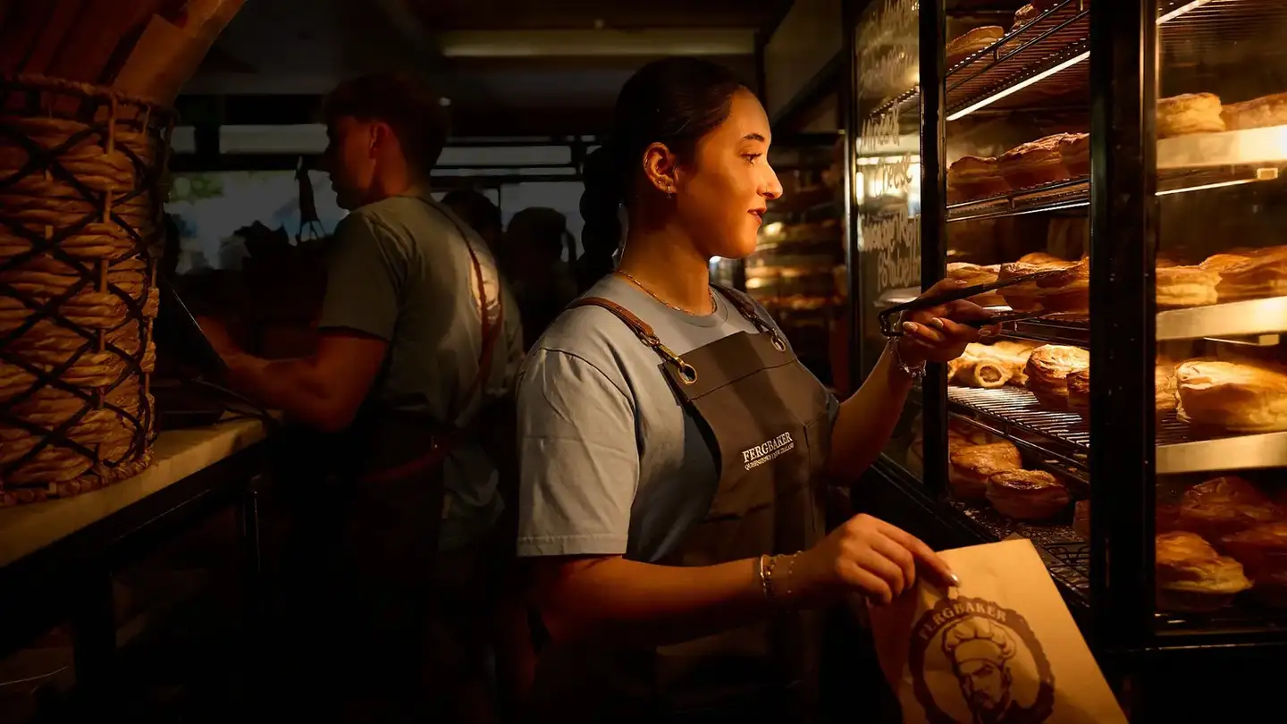 A Fergbaker staff member taking a pie from the lit pastry cabinet into a paper bag