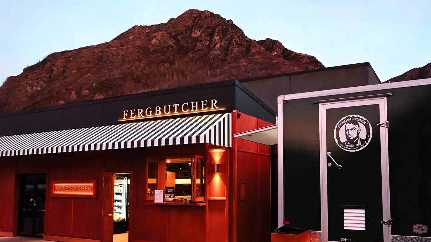 The Fergbutcher shopfront in Arrowtown at dusk, with a striped awning and the hills behind
